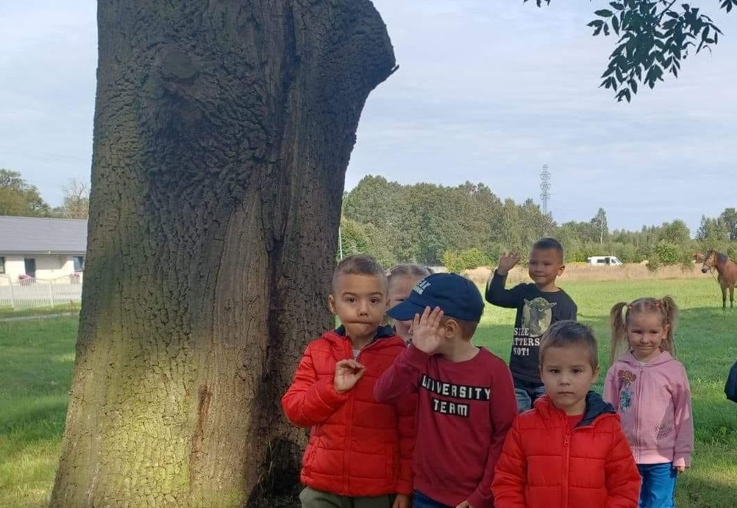 Dzieci stoją w grupie obok drzewa.
