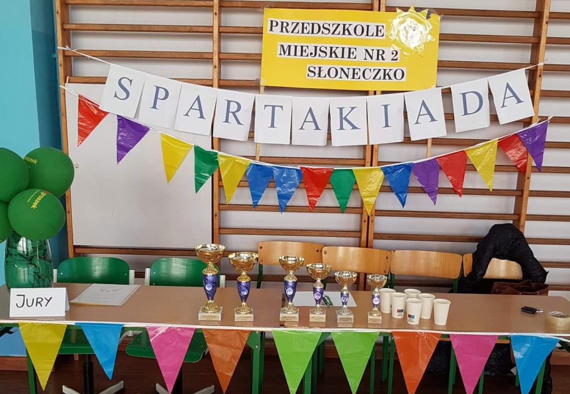 Stół na którym stoją puchary, na drabince zawieszony napis Spartakiada.