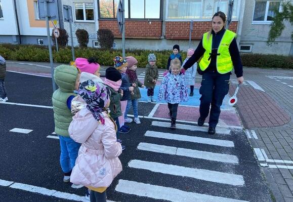 Strażnik Miejski przeprowadza dziecko przez pasy w miasteczku rowerowym.