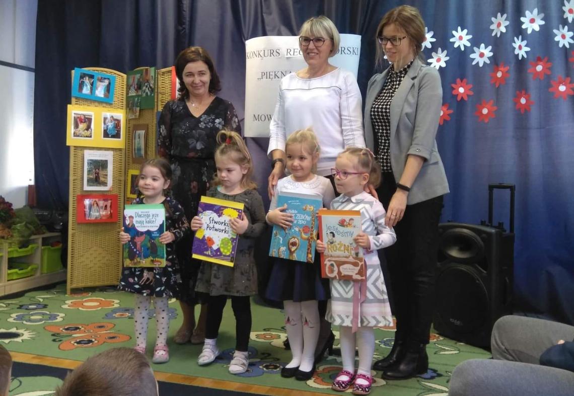 Cztery dziewczynki stoją trzymając książki i dyplomy za zajęte miejsca w konkursie. Za dziewczynkami stoją trzy panie.