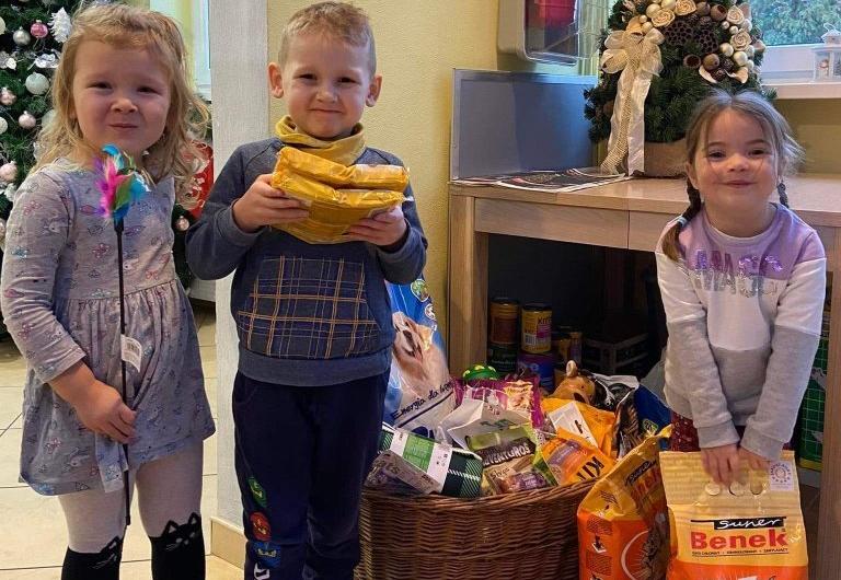 Troje dzieci stoi trzymając w rękach pokarm dla zwierząt.