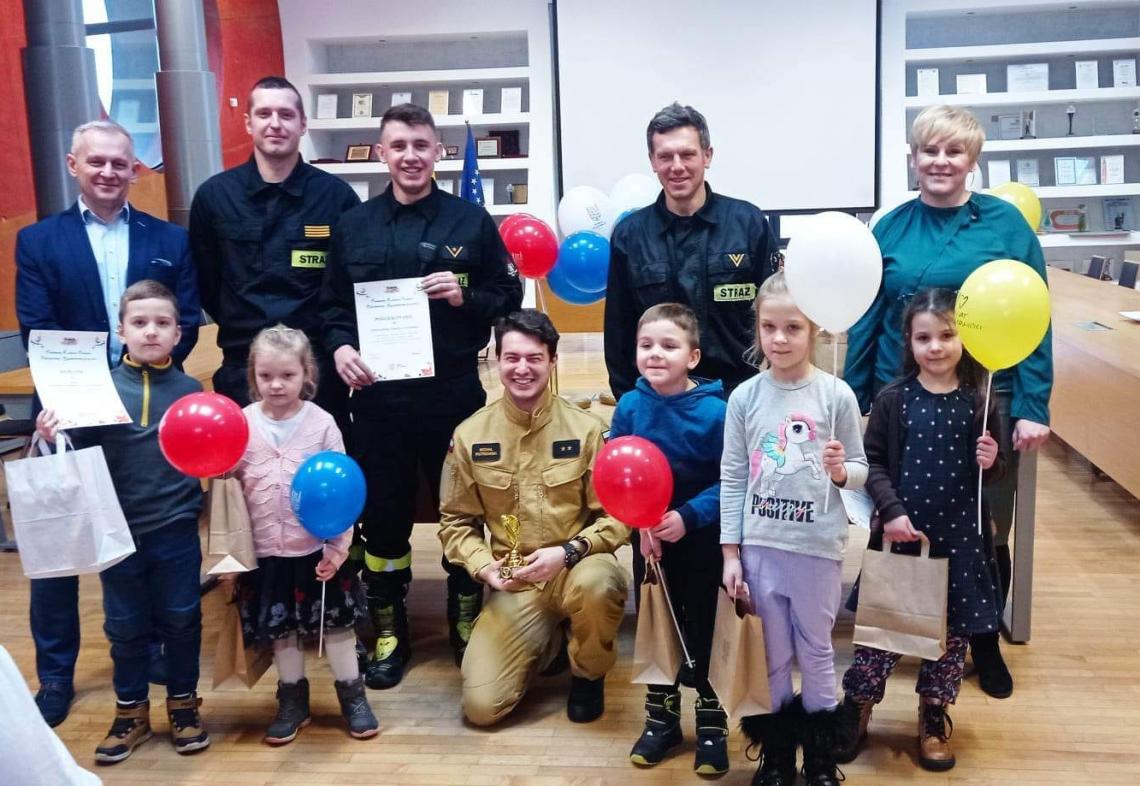 Grupa dzieci ze strażakami. Wręczenie nagród za konkurs.