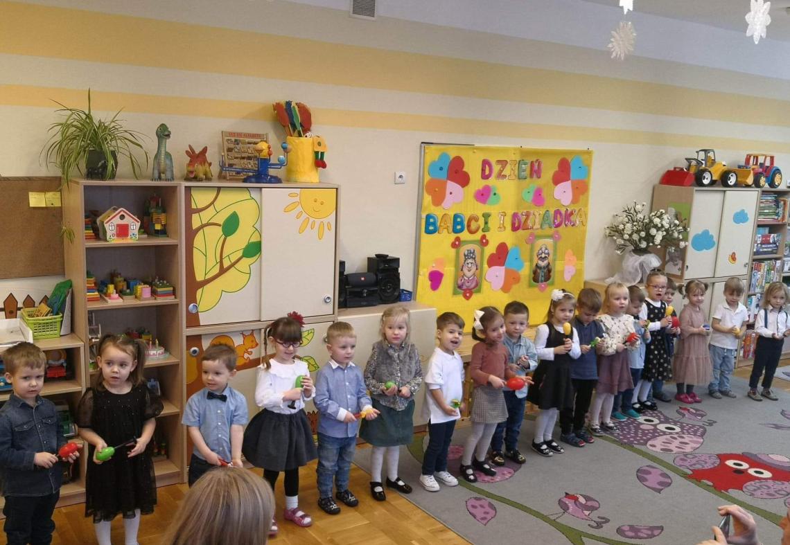 Dzieci stoją w półkolu i śpiewają piosenki dla babci i dziadka.