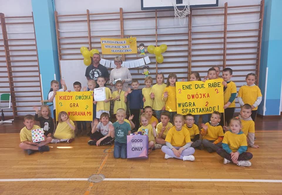 Dzieci ubrane w stroje sportowe pozują do zdjęcia. Jedno dziecko trzyma w ręku puchar.