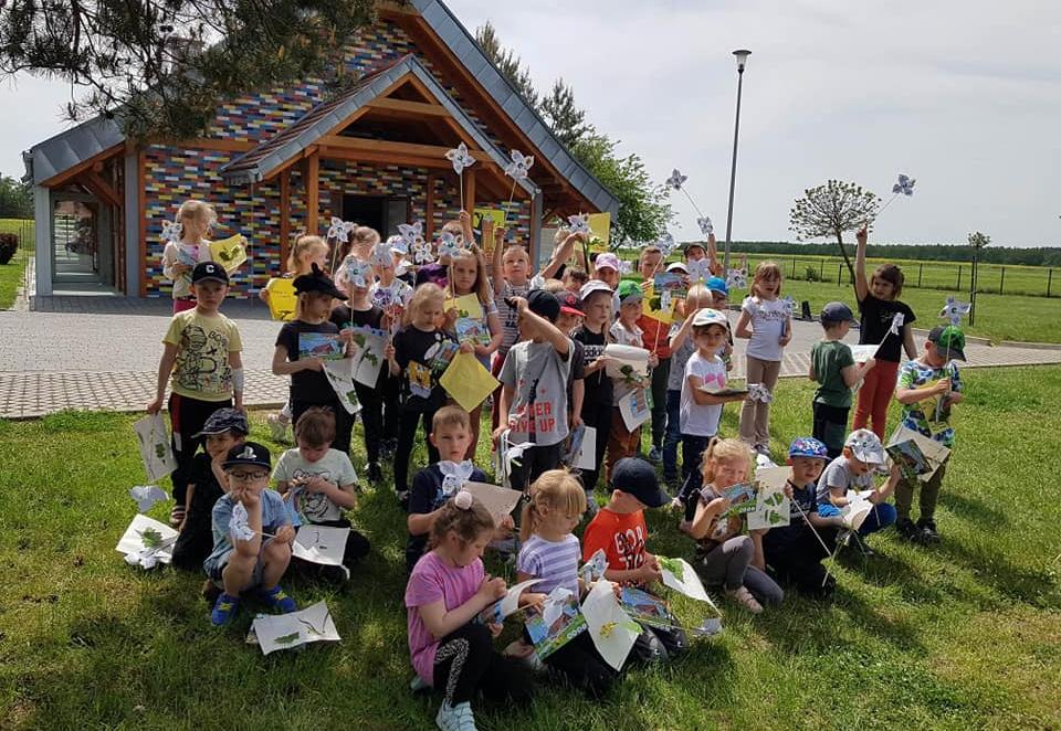 Dzieci stoją w grupie na trawie trzymają w ręku papierowe wiatraki.