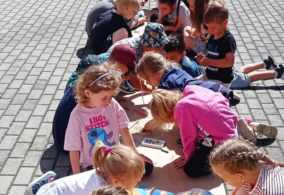 Dzieci są na dworze i rysują na szarym papierze.