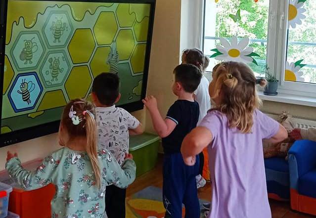 Dzieci ćwiczą przed tablicą interaktywną.