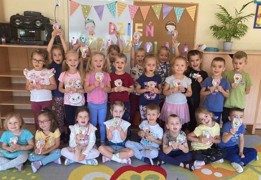 Dzieci stoją w grupie. Trzymają w rękach medale przedszkolaka.