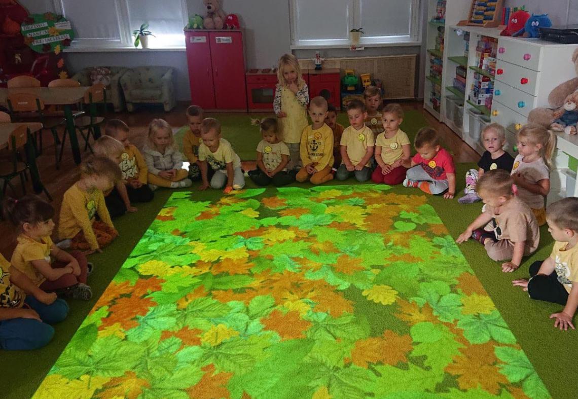 Dzieci siedzą w półkolu na magicznym dywanie.