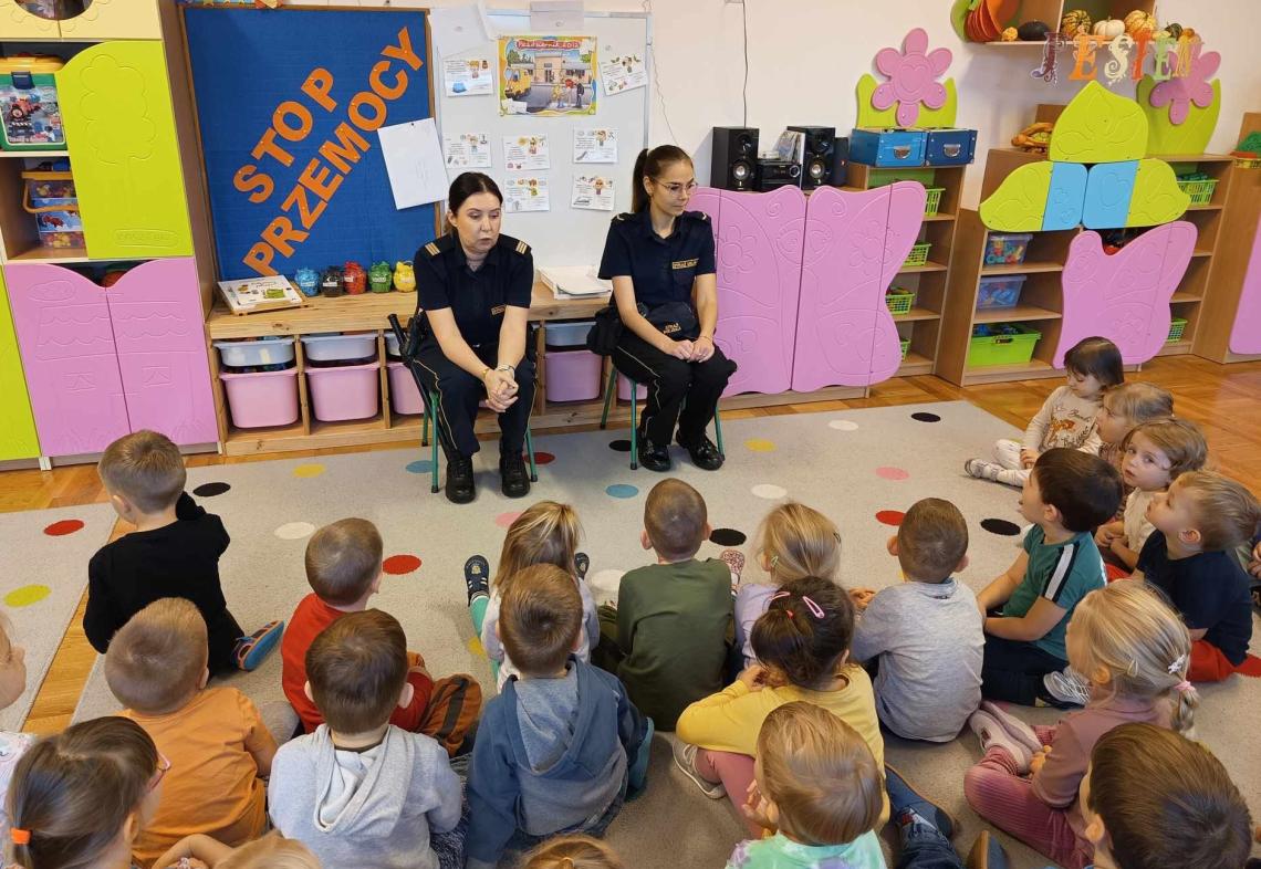 Dzieci siedzą na dywanie na spotkaniu ze strażnikami miejskimi.