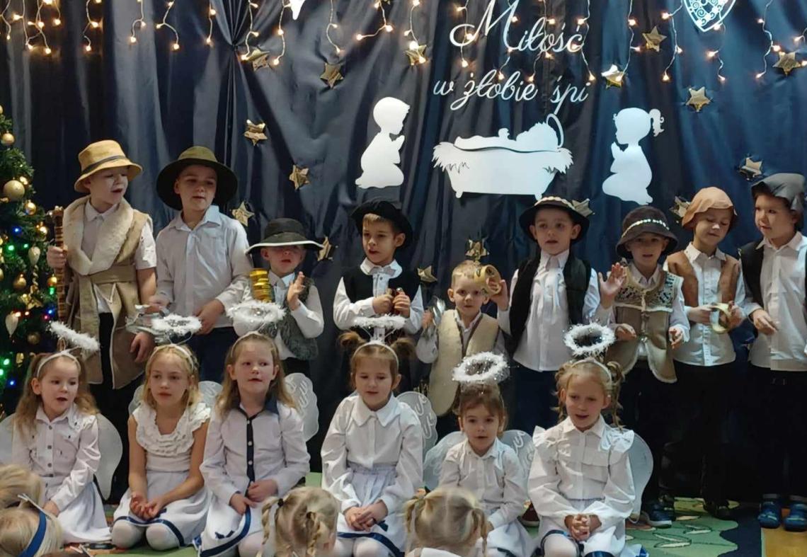 Dzieci przebrane za anioły i pastuszków stoją i śpiewają kolędy.