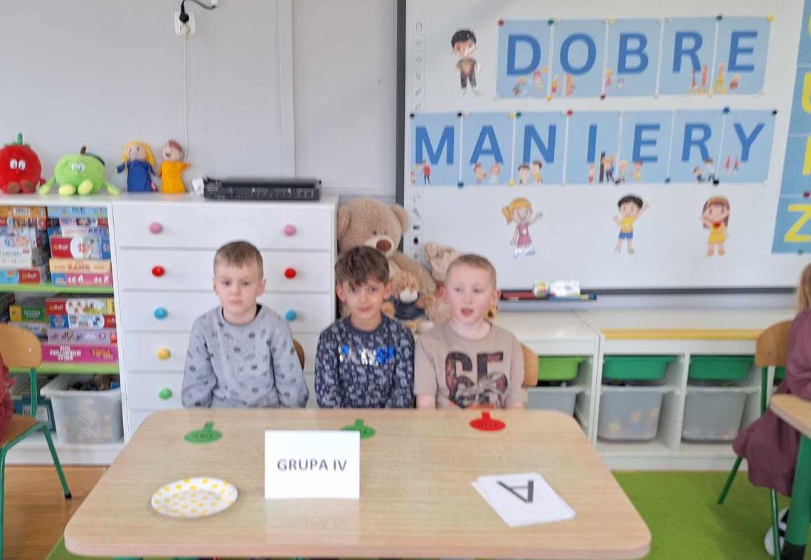 Dzieci siedzą przy stolikach i biorą udział w quizie.