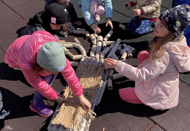 Grupa dzieci na dworze układa obrazek z surowców wtórnych.