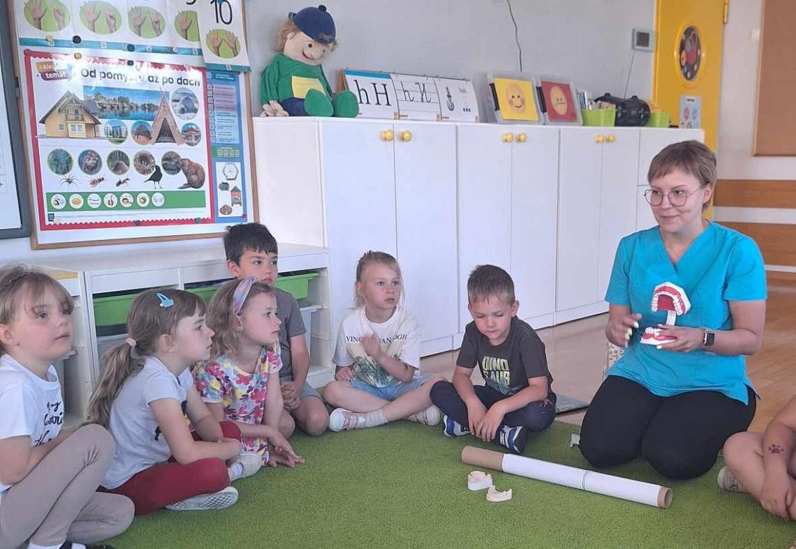 Pani higienistka siedzi z dziećmi na dywanie.