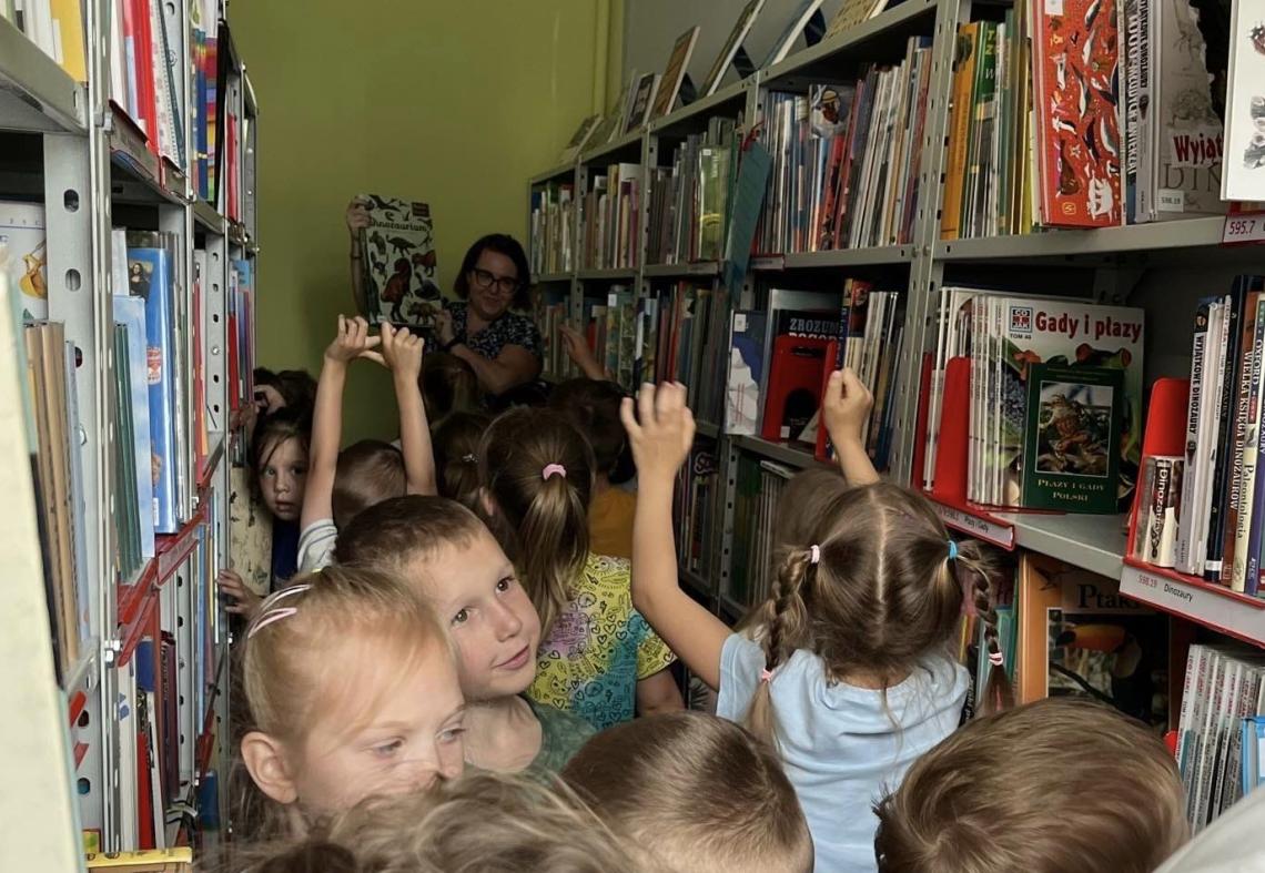 Dzieci stoją pomiędzy regałami z książkami w bibliotece.