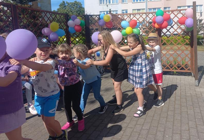 Dzieci tańczą ustawione w pociąg w ogrodzie przedszkolnym.