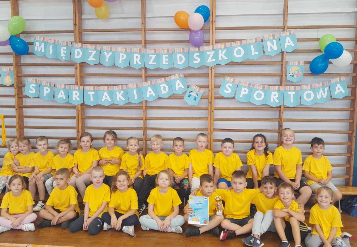 Dzieci ubrane w żółte koszulki pozują do zdjęcia na tle drabinek.