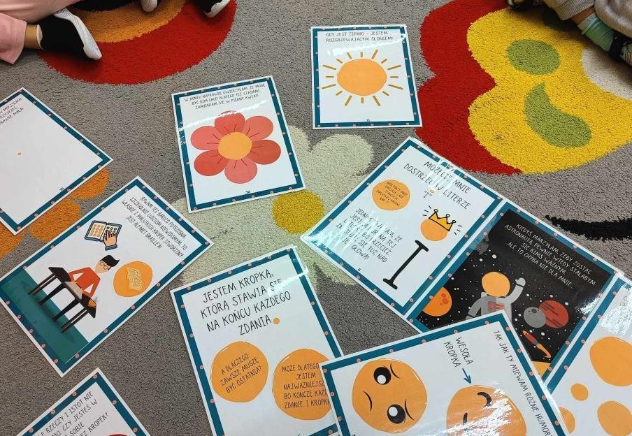 Na dywanie leżą karty przedstawiające historię święta kropki.