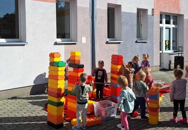 Dzieci bawią się na tarasie przedszkolnym dużymi klockami.