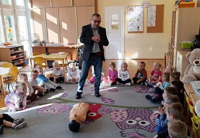 Na dywanie leży fantom, dzieci siedzą w kole słuchając pana.