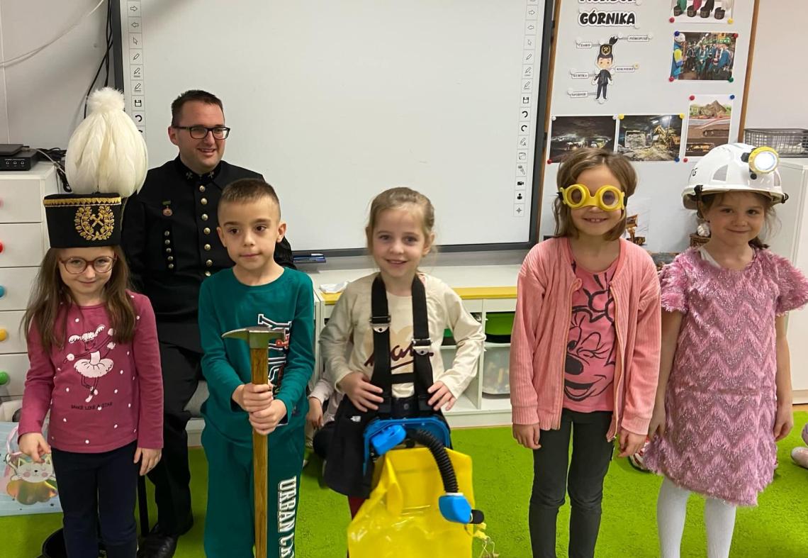 Czworo dzieci stoi w górniczych czapkach razem z górnikiem.