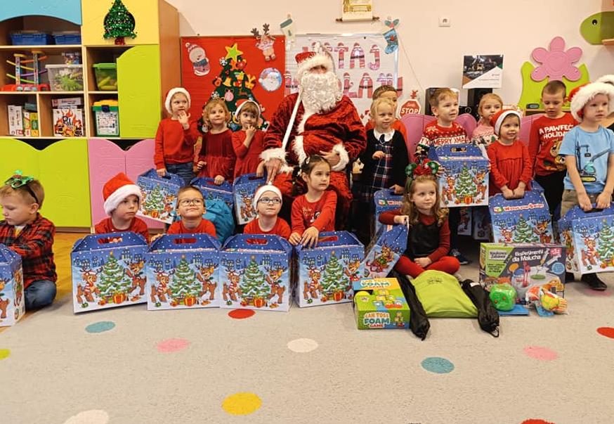 Dzieci ubrane na czerwono, trzymają w ręku paczki, pozują do zdjęcia z mikołajem