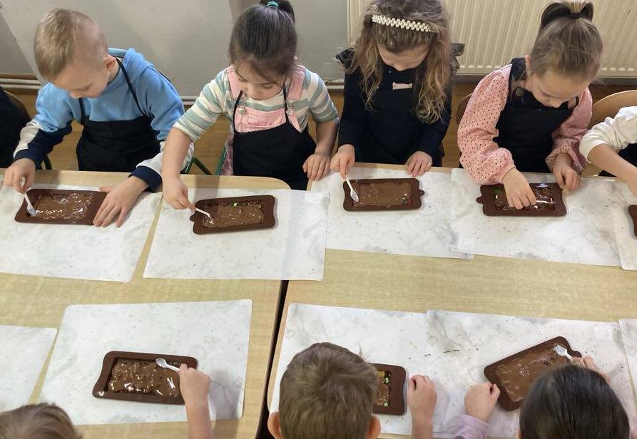 Dzieci siedzą przy stole i tworzą swoją czekoladę.