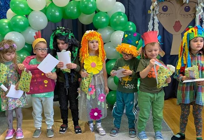 Dzieci ubrane w stroje zrobione z surowców wtórnych stoją w rzędzie z dyplomami i upominkami.i 