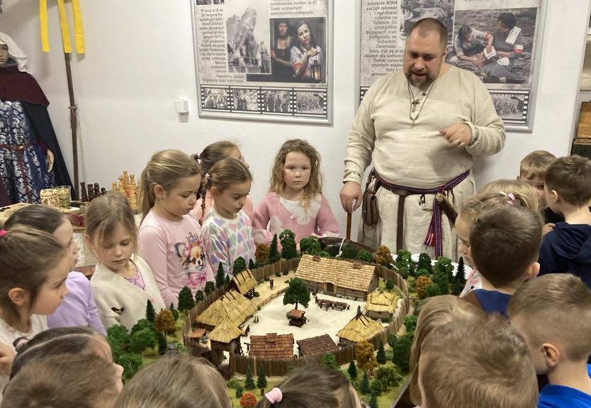 Dzieci stoją wokół stołu, na którym jest makieta grodu.