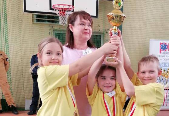 Troje dzieci ubranych w żółte koszulki i Pani trzymają wspólnie puchar.