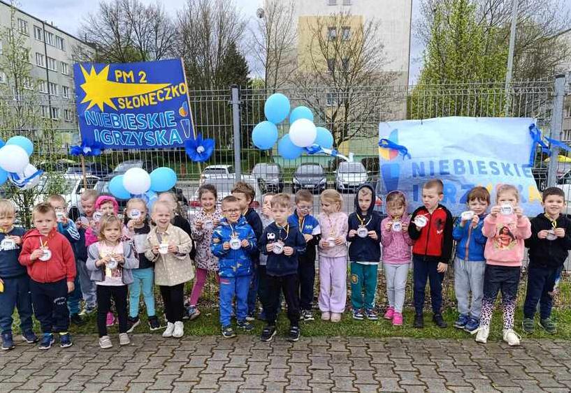 Dzieci stoją w grupie za nimi plakat z napisem niebieskie igrzyska.