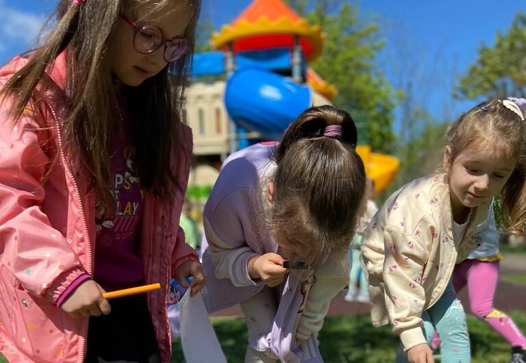 Trzy dziewczynki szukają z lupami owadów na trawie.