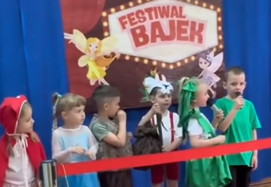 Dzieci przebrane za postacie z bajek stoją na czerwonym dywanie.