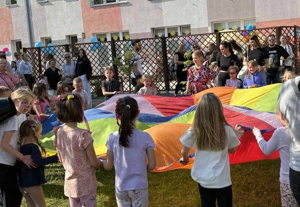 Dzieci wraz z rodzicami trzymają kolorową chustę animacyjna w ogrodzie przedszkolnym.