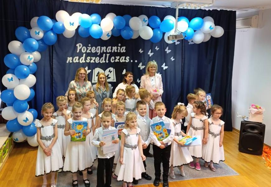 Dzieci ubrane na galowo stoją w grupie razem z Paniami i pozują do zdjęcia.