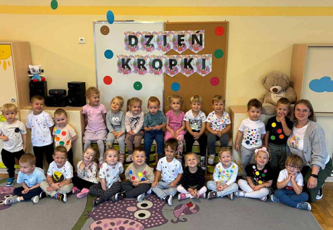 Dzieci ubrane w bluzeczki z kropkami pozują do zdjęcia razem z panią.