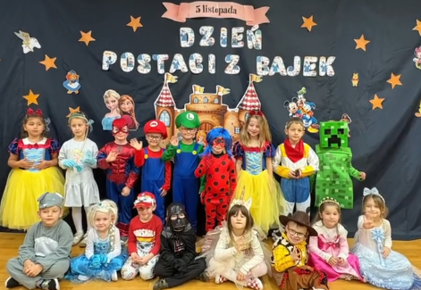 Dzieci przebrane za postacie z bajek pozują do zdjęcia na niebieskim tle z napisem dzień postaci z bajek.