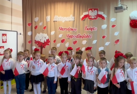 Dzieci ubrane na galowo stoją w grupie trzymając w ręku flagi Polski