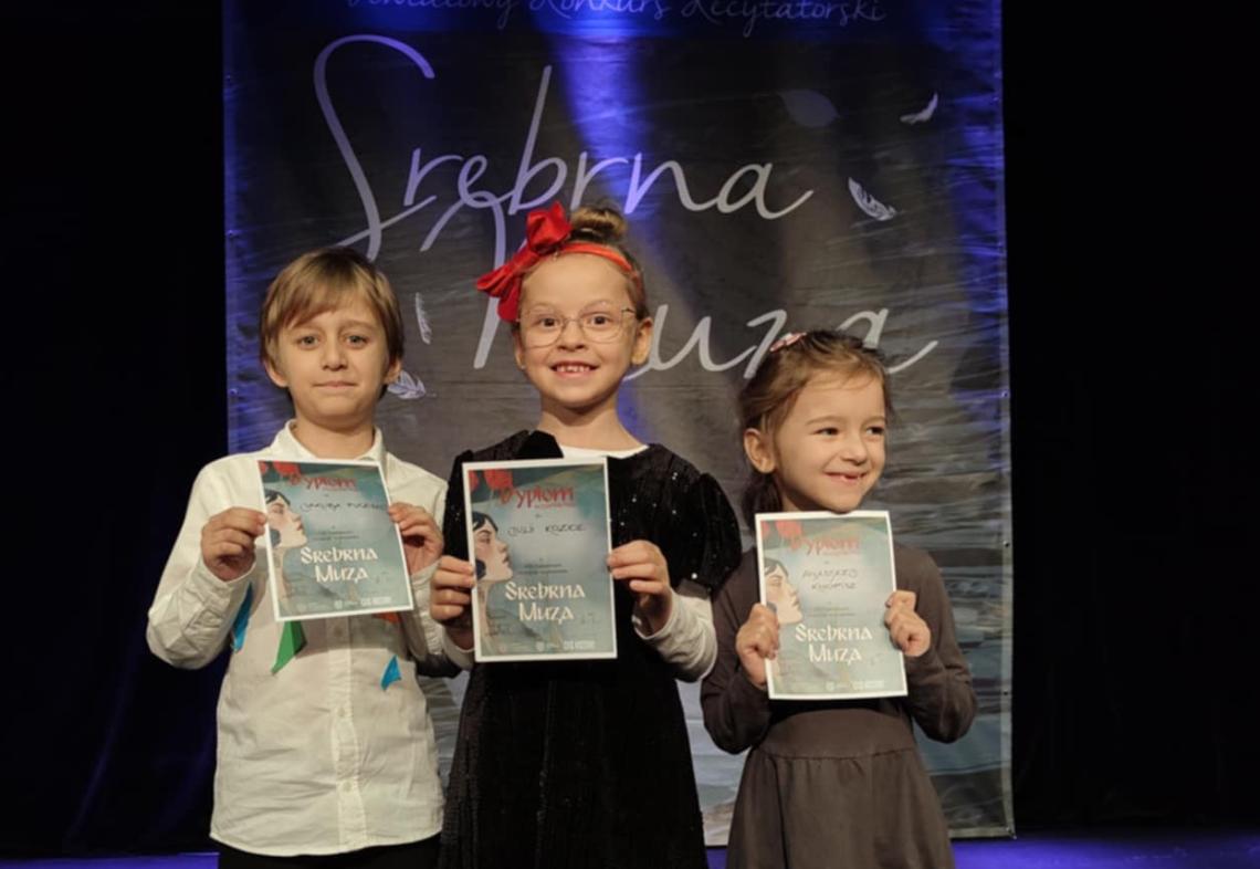 Troje dzieci stoi na scenie z dyplomami.
