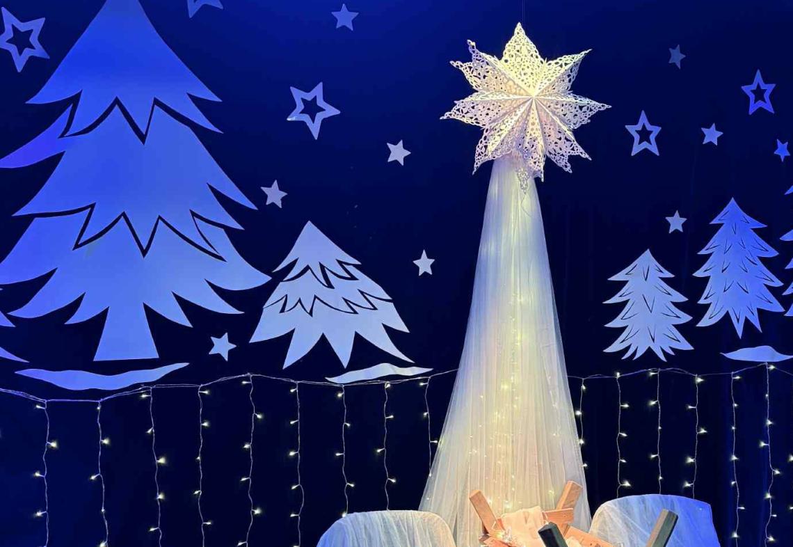 Na scenie białe choinki przyczepione do kotary, stoi żłobek i gwiazda betlejemska.