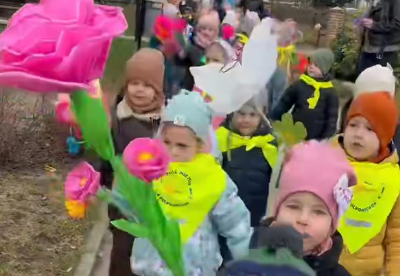 Dzieci idą w parach trzymając w rękach kolorowe kwiaty.