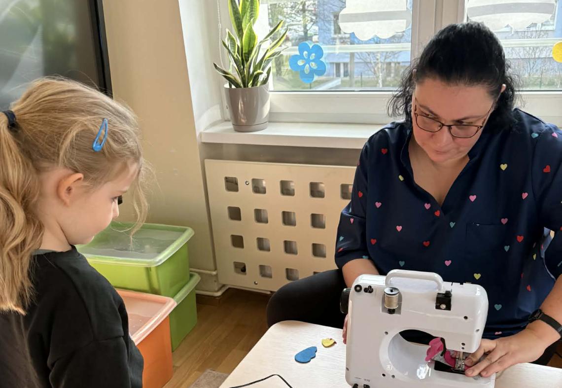 Pani szyje na maszynie dziewczynka stoi obok.