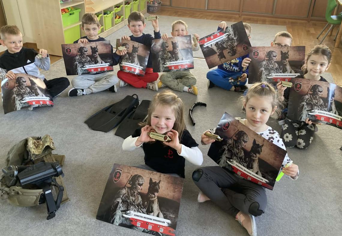 Dzieci siedzą na dywanie trzymając w rękach  przedmioty oraz obrazki związane z wojskiem.