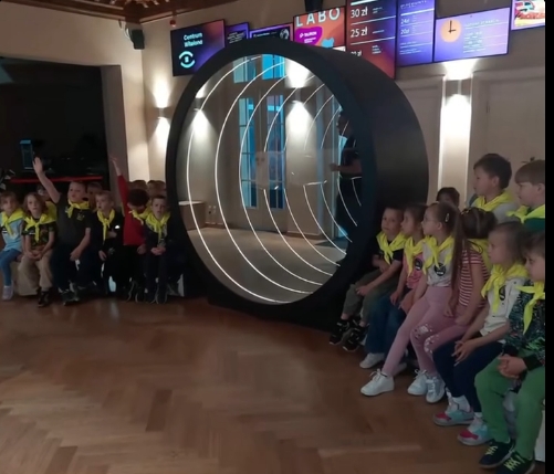 Dzieci siedzą w grupie koło makiety oka.