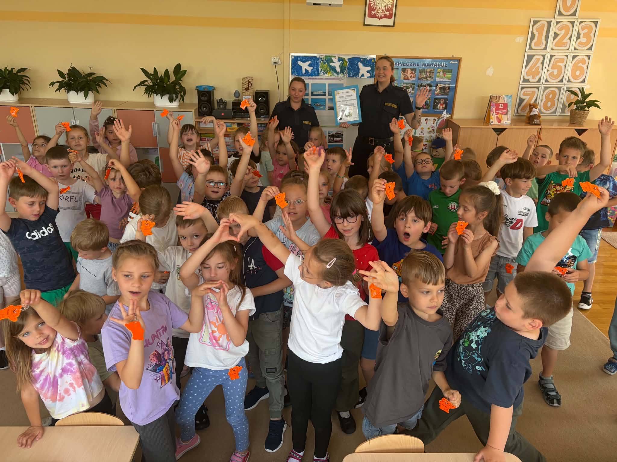 Dzieci stoją w grupie razem z paniami ze straży miejskiej w ręku trzymają odblaski.