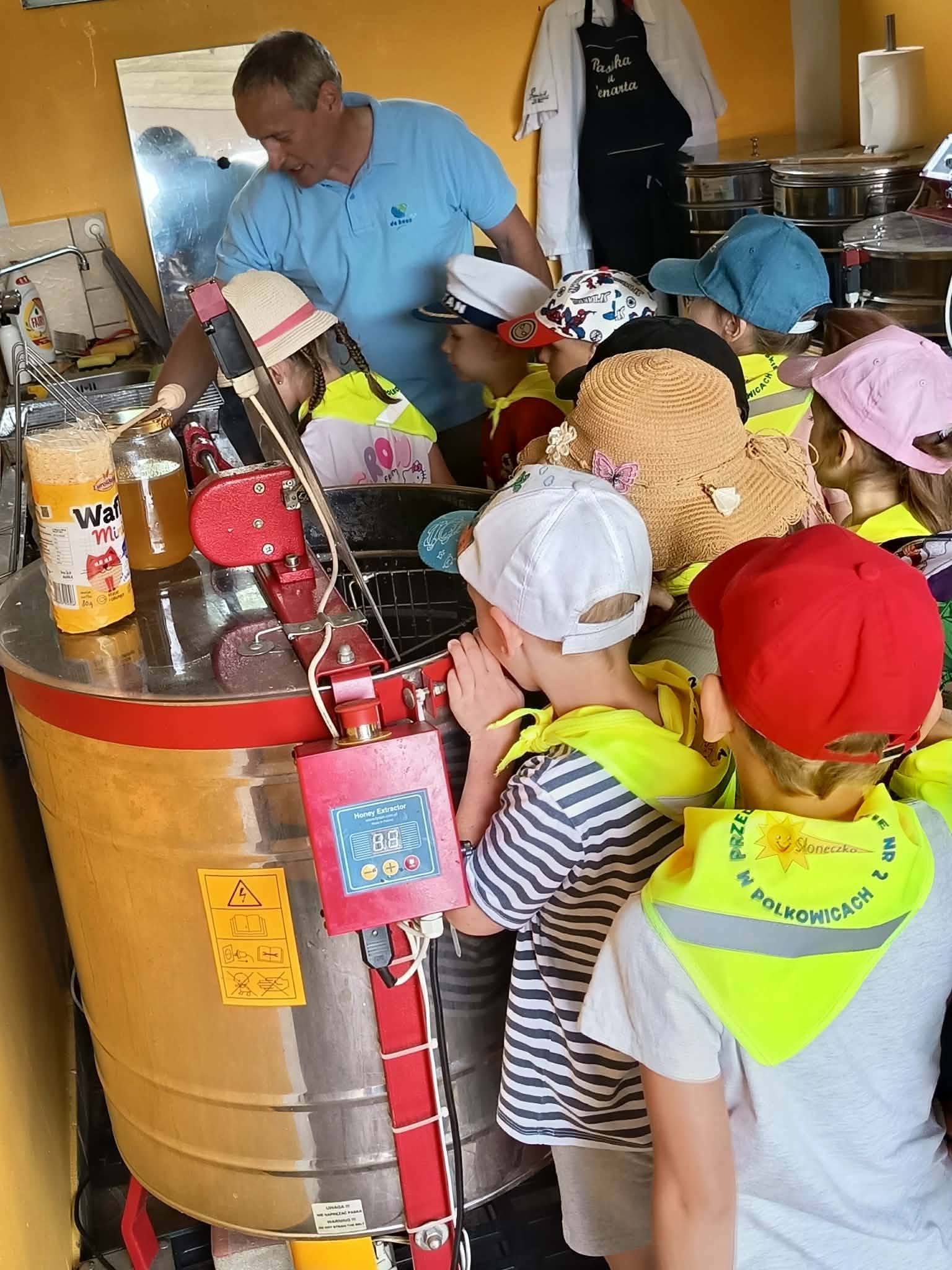 Grupa dzieci patrzy jak Pani opowiada jak powstaje mi&oacute;d.