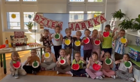 Dzieci pozują do zdjęcia na tle napisu dzień jabłka trzymając w rękach wykonane przez siebie papierowe jabłka.