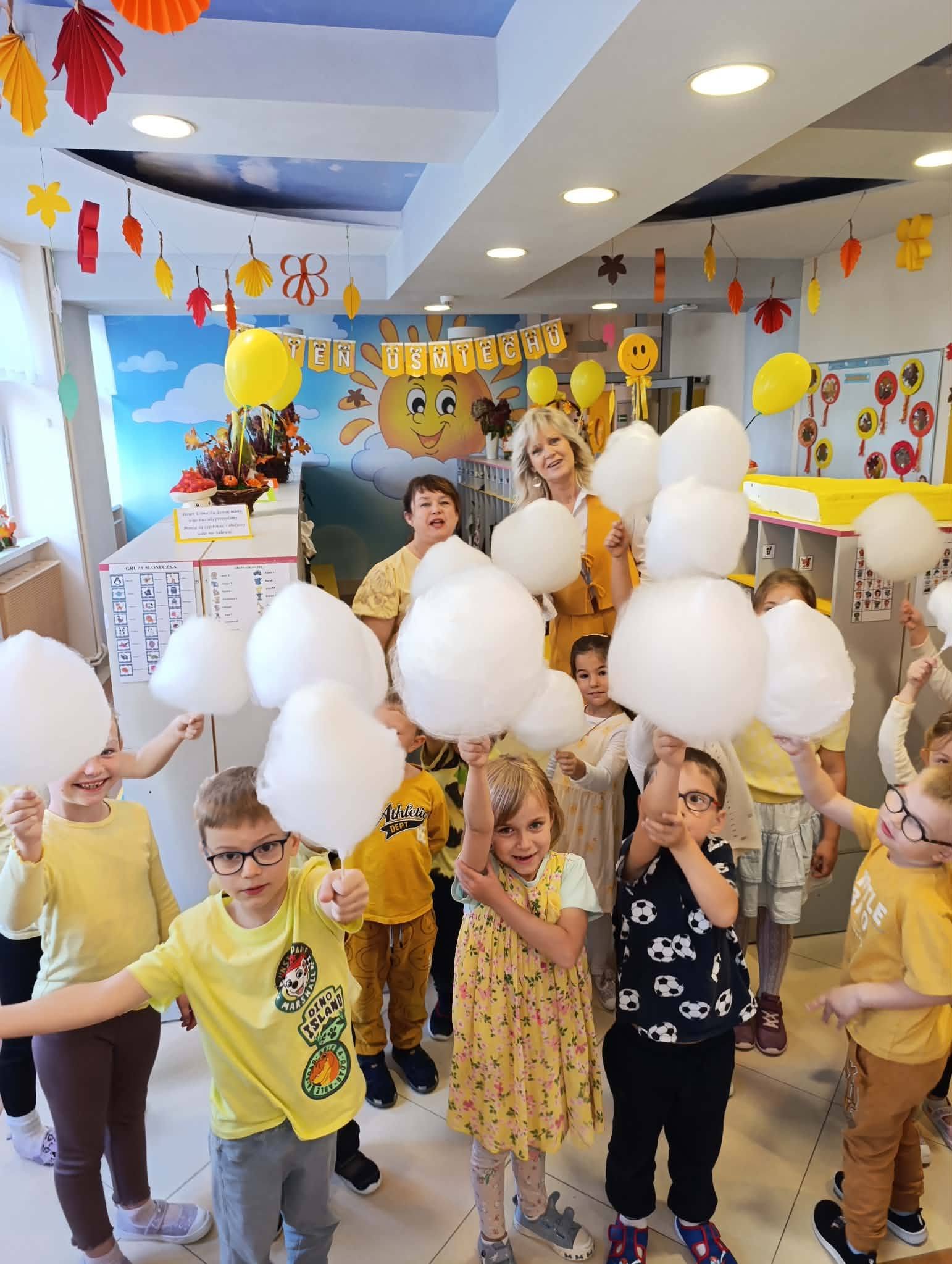 Dzieci ubrane na ż&oacute;łto stoją w grupce trzymając w rękach watę cukrową.   