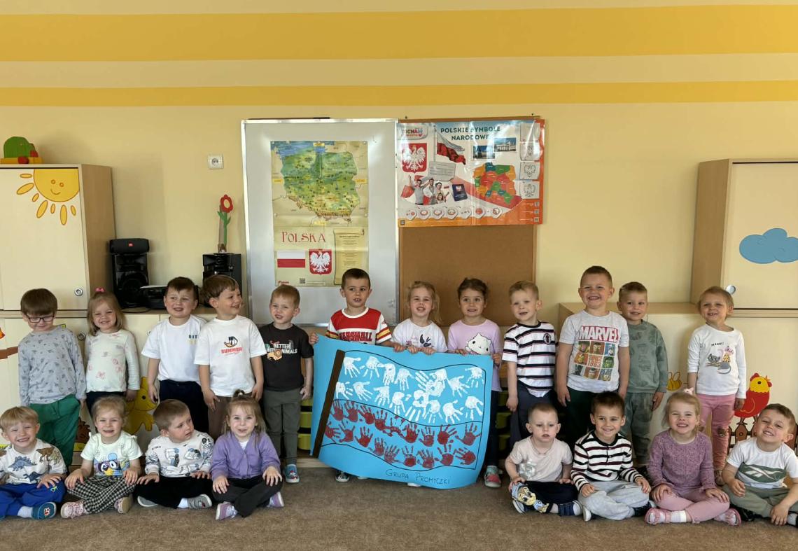 Dzieci pozują do zdjęcia trzymając w rękach plakat z flaga Polski.