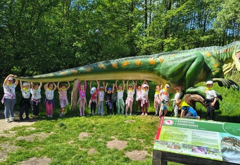 Dzieci stoją w rzędzie pod dinozaurem.